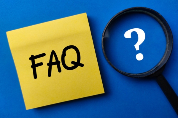 FAQ written on yellow sticky note beside a magnifying glass enhancing a question mark