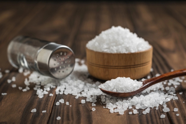 Glass salt shaker, wooden Cup and spoon with salt on the table depicting salt and resin for water softener