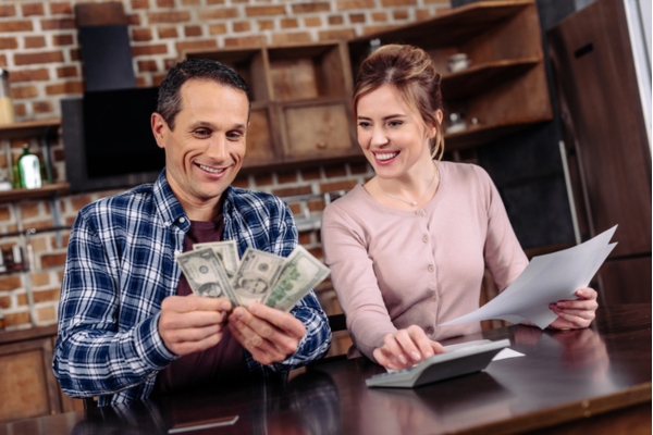 happy couple smiling while counting money and computing expenses depicting cost benefits