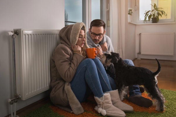 image of a couple and their dog feeling cold indoors sitting by the heating radiator depicting Frozen fuel oil symptoms