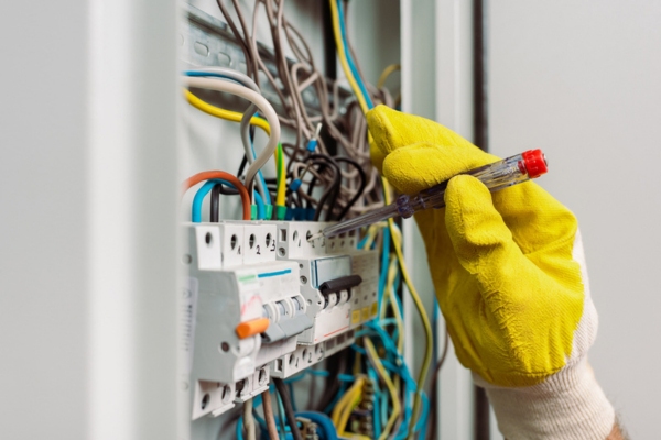 image of an electrician's hand holding a screwdriver while fixing an electrical panel