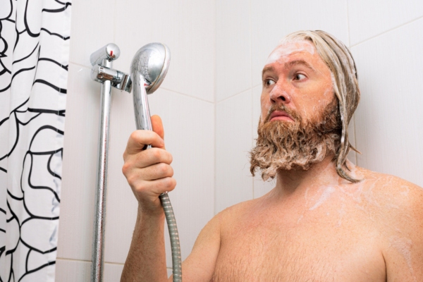 man looking at shower head with hair full of shampoo due to water interruption