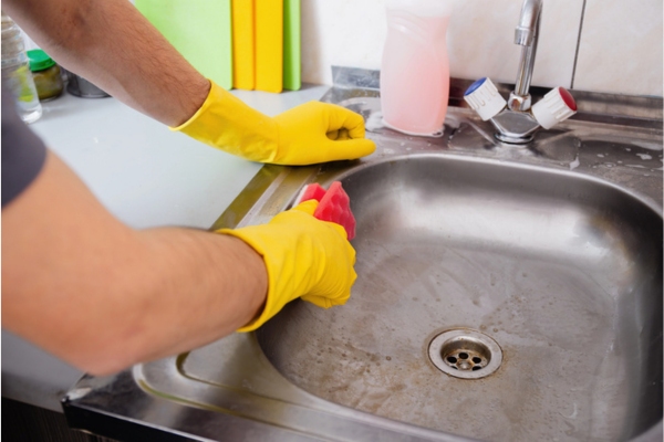 Man in gloves scrubbing and cleaning kitchen sink