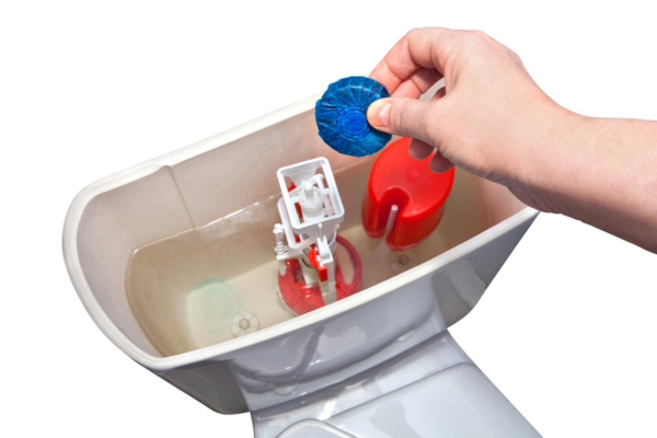 cropped view of a homeowner's hand about to drop an in-tank cleaner in a toilet bowl