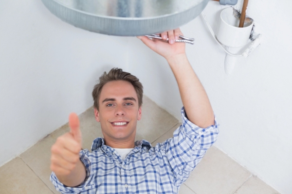 plumber inspecting hot water heater while doing a thumbs up