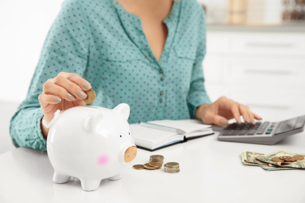 cropped view of a woman counting cash and putting money in a piggy bank depicting controlling heating oil costs